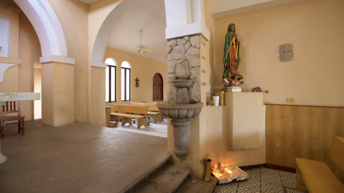 Interior of the Church of Saint Luke in Cabo San Lucas with arches, wooden benches, and religious statues.