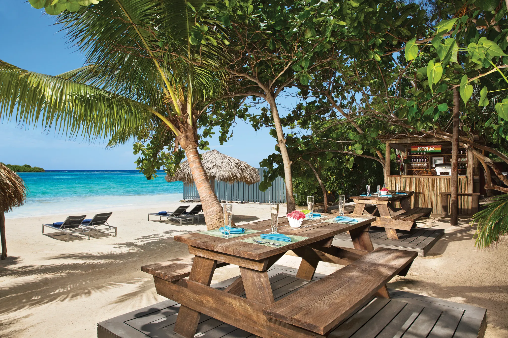 Jerky Jo’s beachside restaurant at Zoëtry Montego Bay Jamaica featuring outdoor Jamaican jerk dining, picnic tables, palm trees, and turquoise Caribbean Sea views.