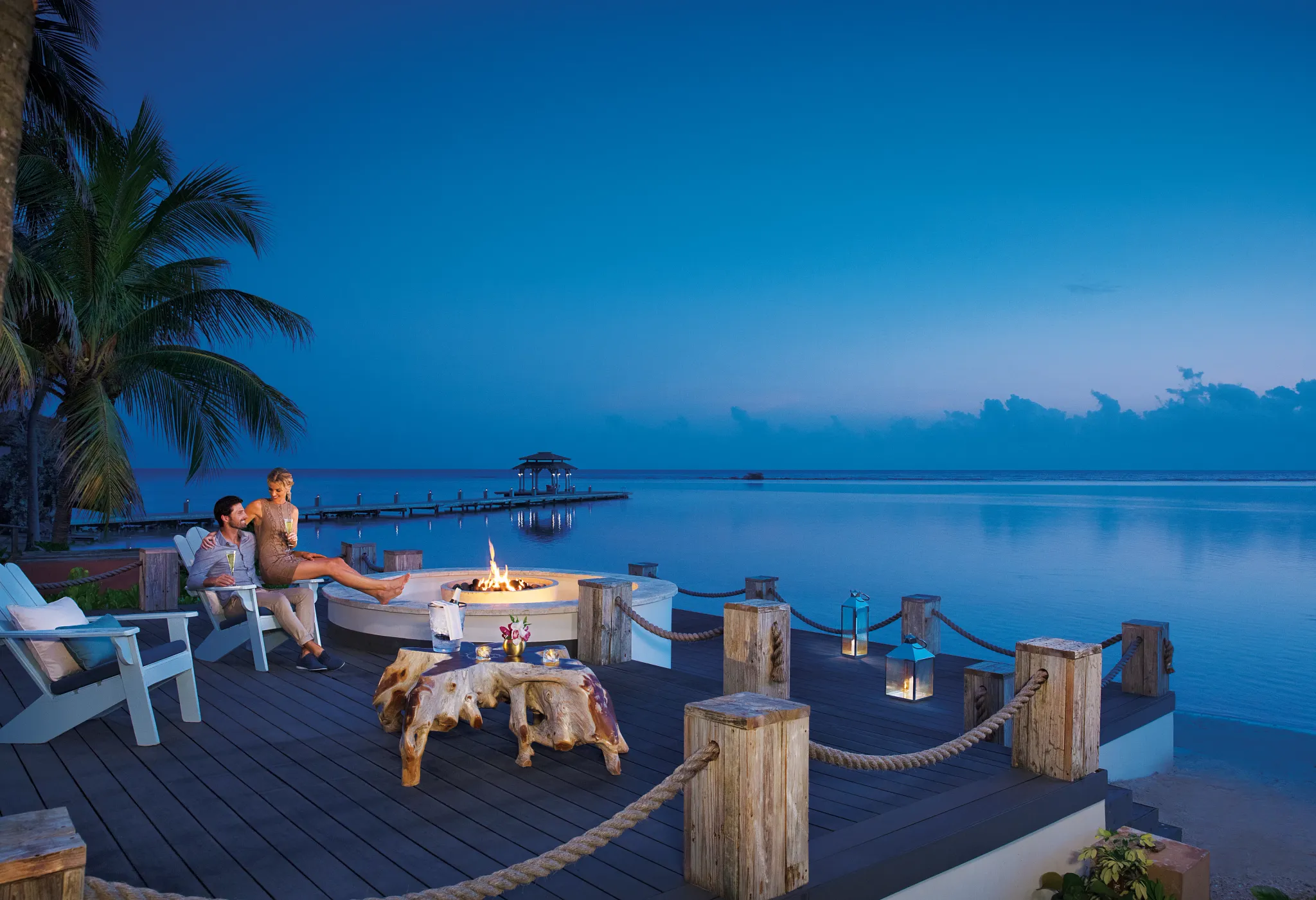 Couple enjoying drinks by an oceanfront firepit at Zoëtry Montego Bay Jamaica at dusk.