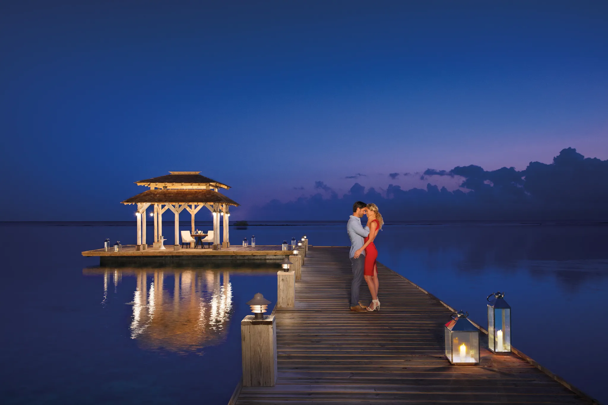 Couple embracing on a private pier at sunset at Zoëtry Montego Bay Jamaica with a candlelit gazebo over the Caribbean Sea.